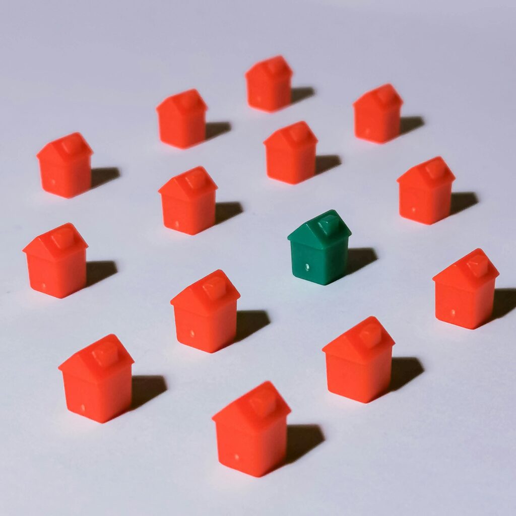 Miniature red and green monopoly houses on a white backdrop emphasizing contrast and arrangement.