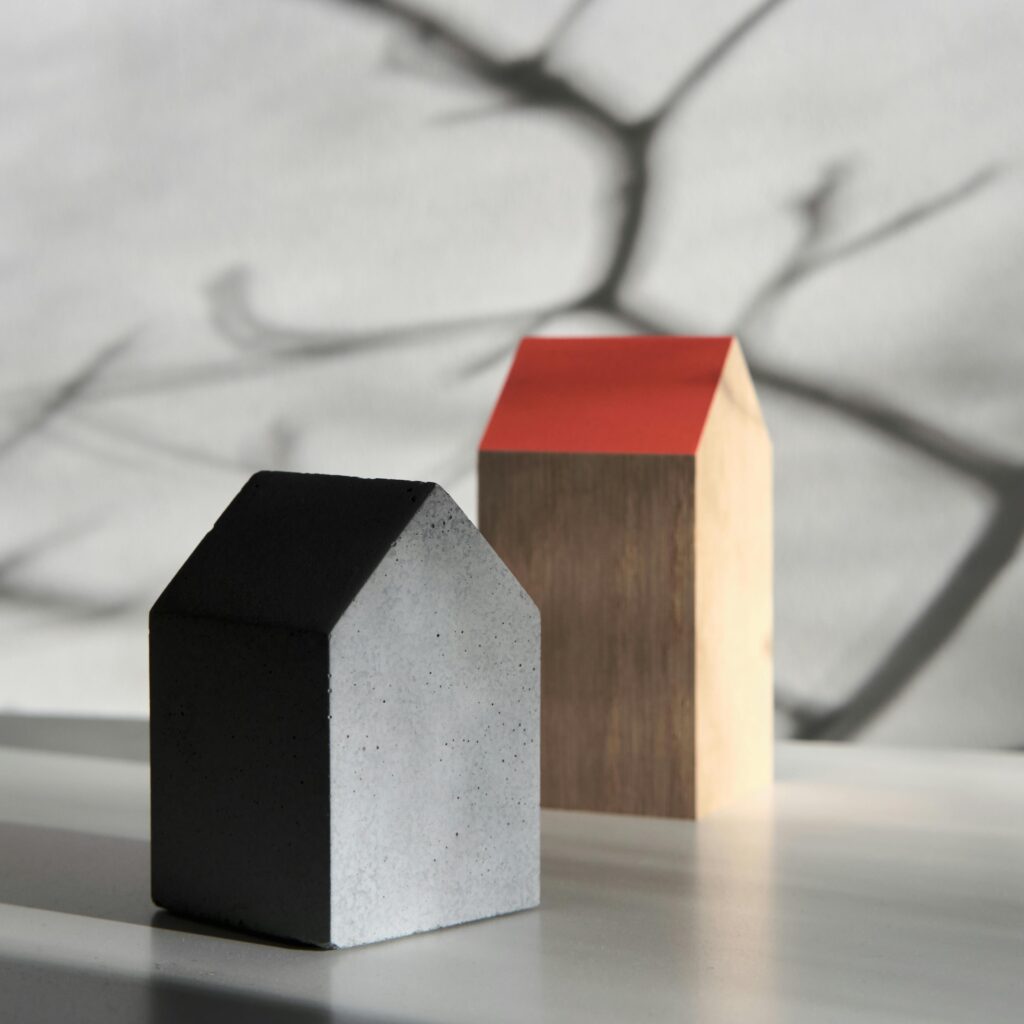 Two minimalist model houses set against a backdrop of dramatic shadows on a wall.